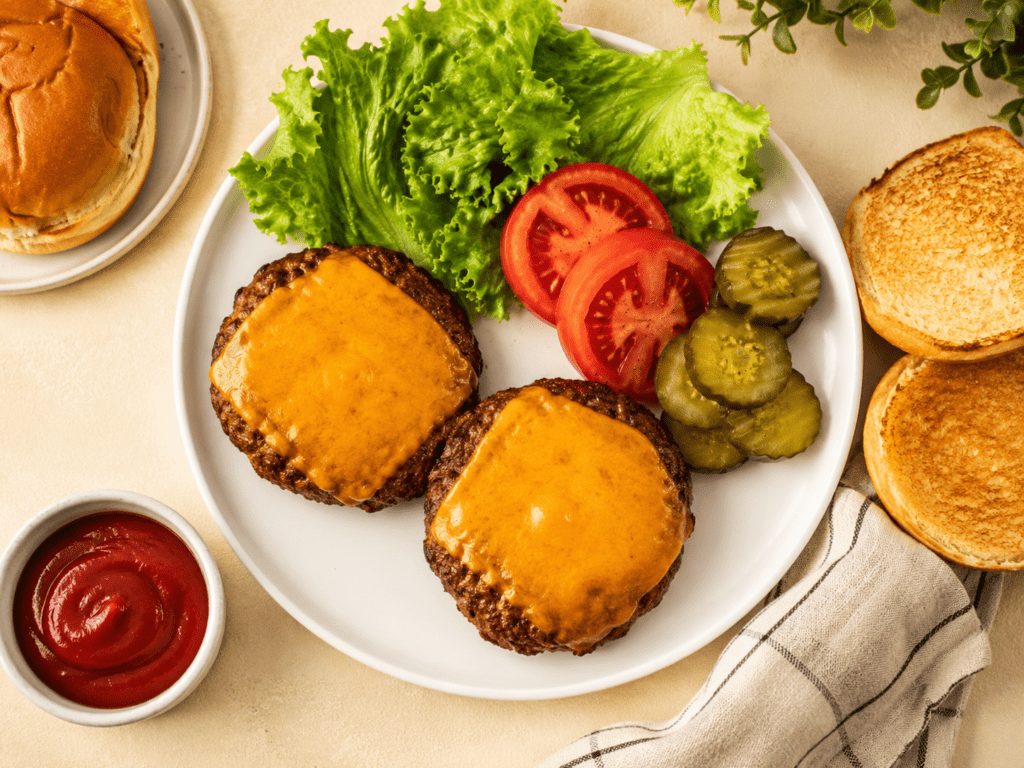 golden air fryer frozen burgers with melted cheese fresh lettuce tomato pickles and toasted buns on a white plate